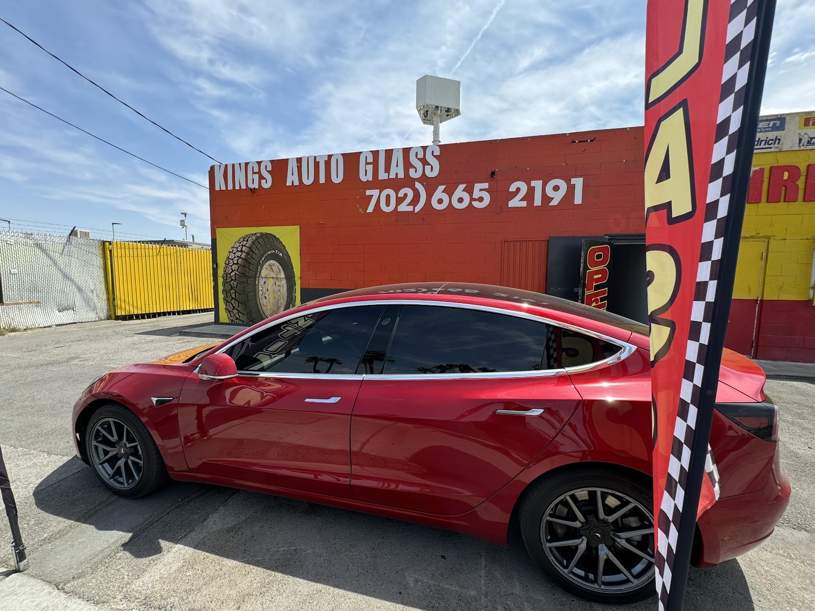 Red Tesla Model 3 with tinted windows parked in front of the Kings Auto Glass building